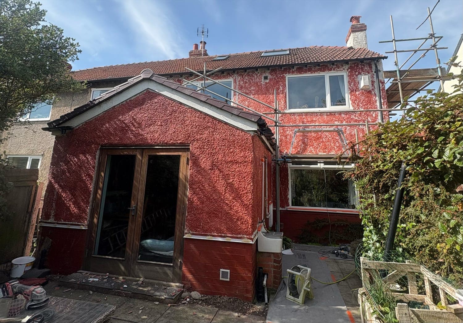 Rear of a semi-detached house in tired red-painted pebbledash, scaffold in place