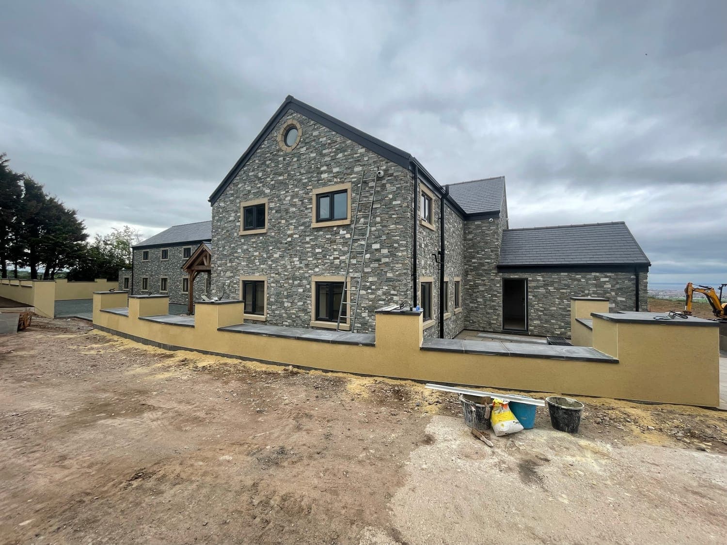 Stone-faced new build with monocouche-rendered boundary walls and stone copings