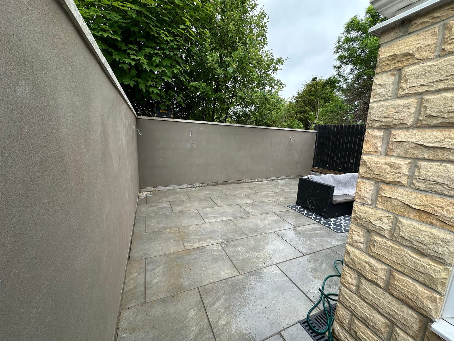 Garden wall finished in smooth render, returning into a stone-clad pier beside a sandstone patio