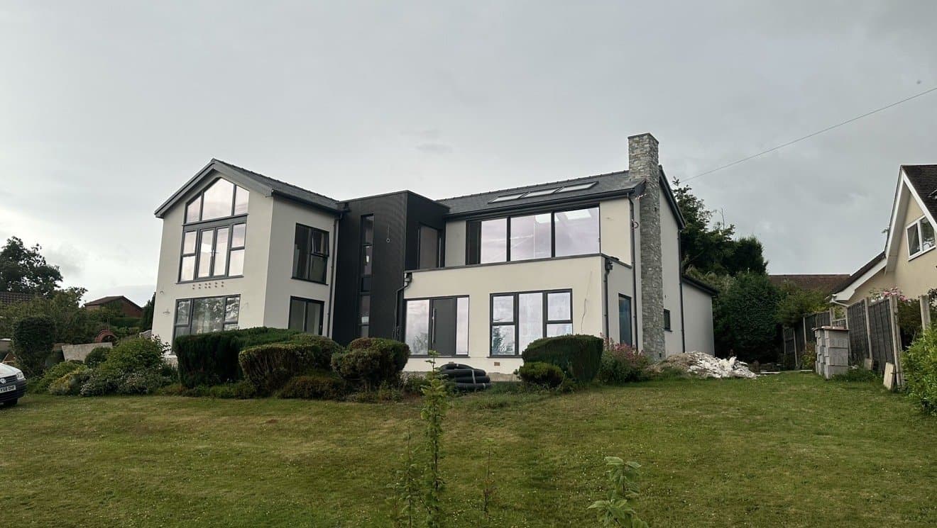The same house after completion, finished in cream monocouche render with dark grey feature panels
