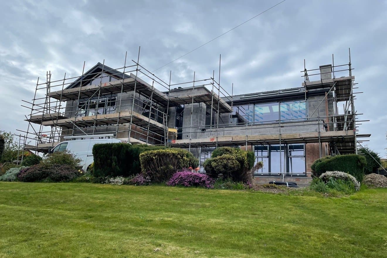 Detached house under scaffold before rendering, with bare blockwork elevations