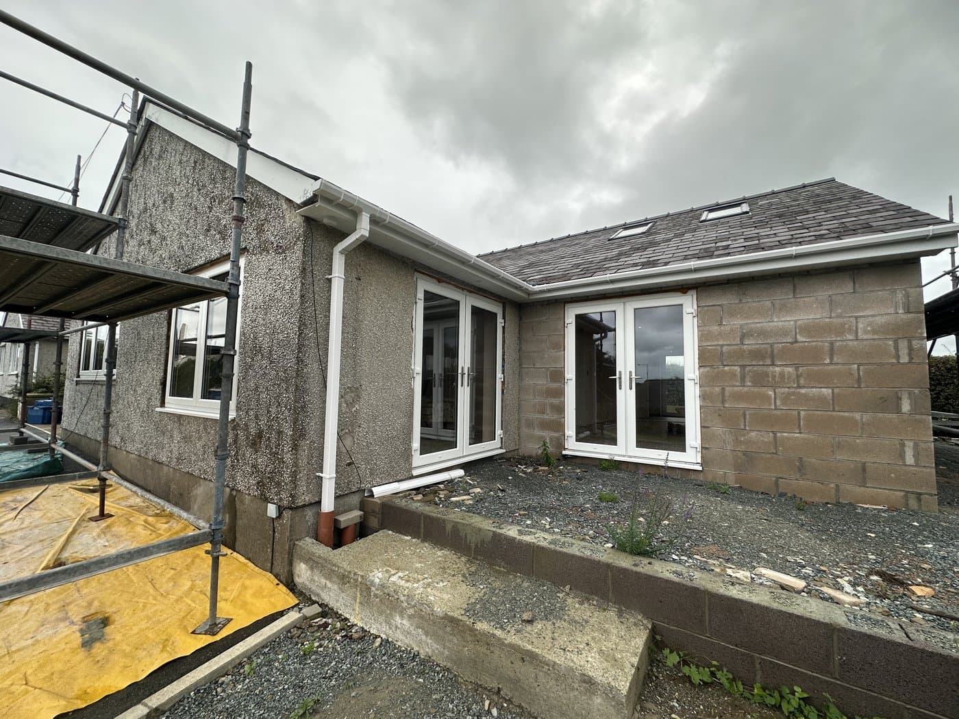 Bungalow with tired pebbledash render being stripped back, scaffold in place