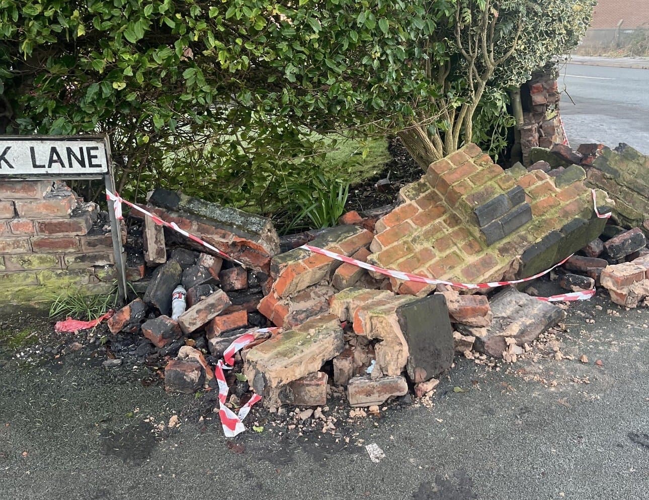 Collapsed roadside brick wall behind hazard tape, rubble across the pavement