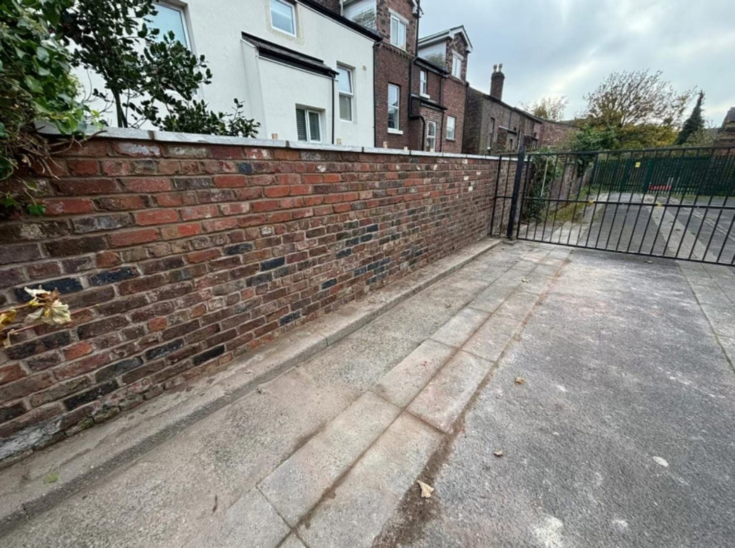 Rebuilt brick boundary wall running the length of a driveway, with railings and gates at the end
