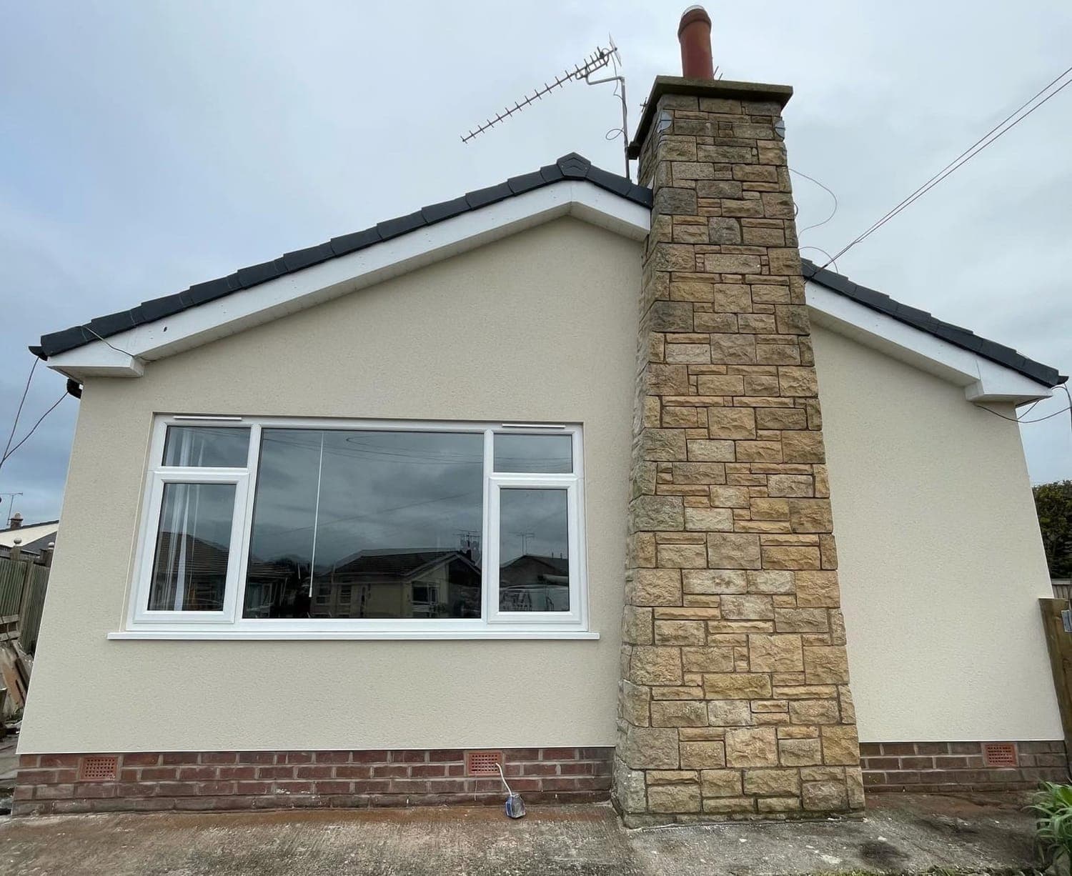 Bungalow finished in cream monocouche render, with a stone-clad chimney breast left exposed