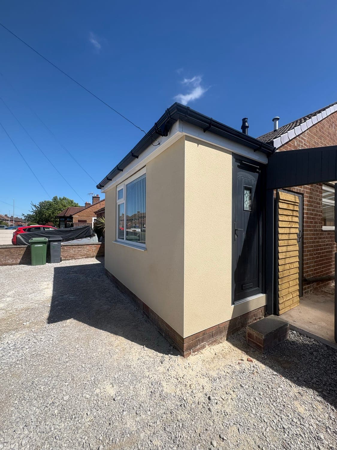 Single-storey extension finished in cream monocouche render against a dark grey front door