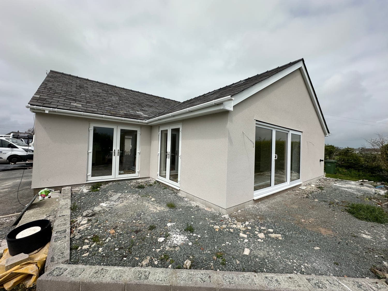 Corner of a bungalow finished in off-white silicone render, with bi-fold doors and white uPVC windows