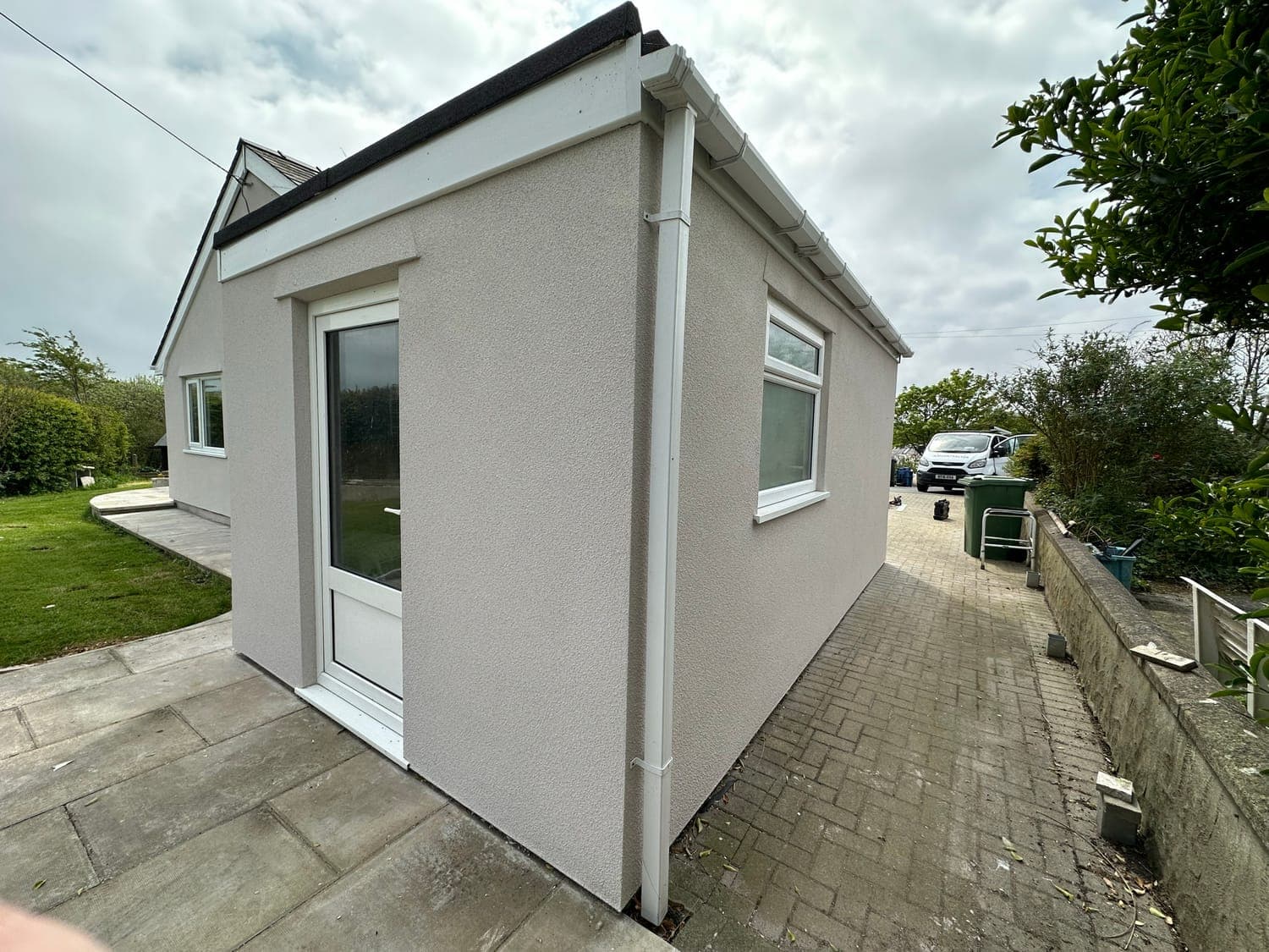 Single-storey extension in pale silicone render, showing the clean bell-cast detail at the base