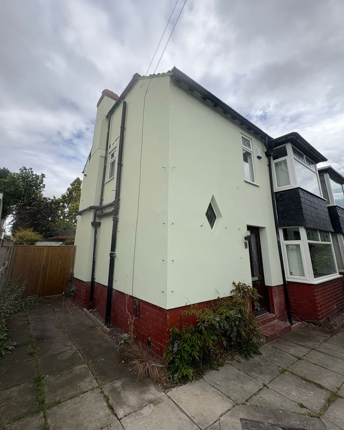 Semi-detached house re-rendered in pale green silicone render above the original red brick plinth