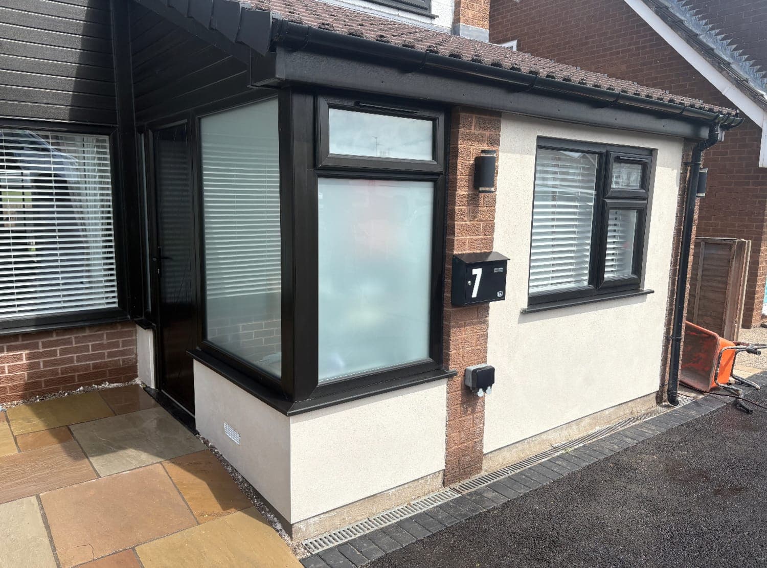 Smooth-rendered bay and porch in off-white, with dark grey window frames and a sandstone path